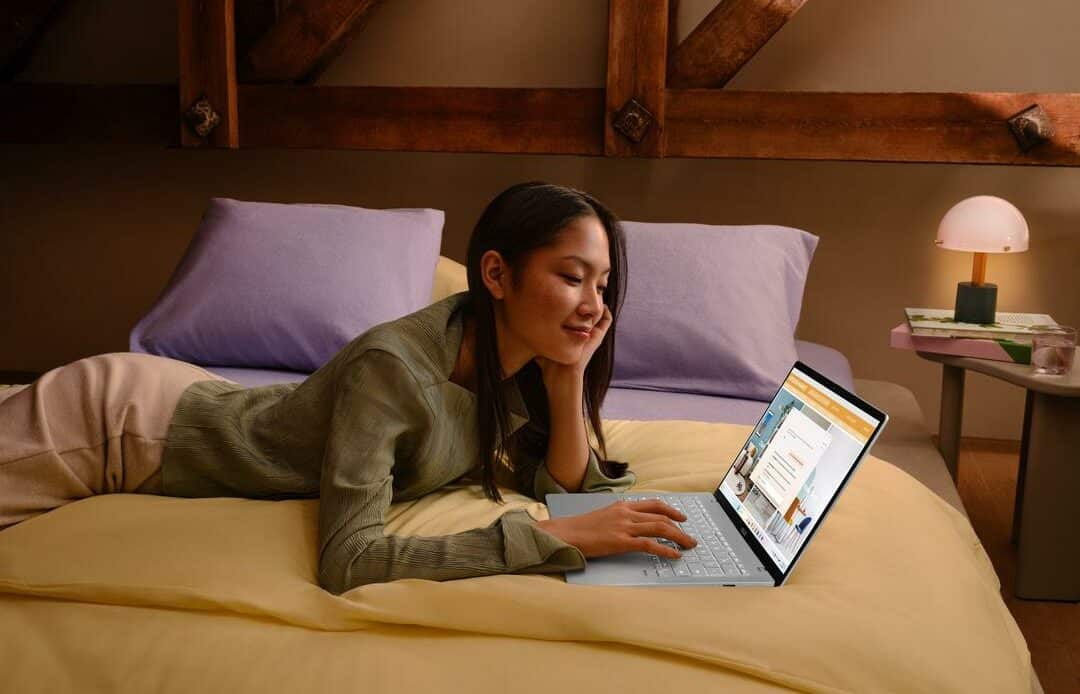 Mulher deitada na cama, usando o notebook vivobook s14, idealizado como o melhor notebook para estudar, em um ambiente aconchegante.