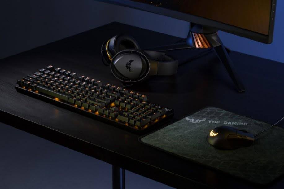 Acessórios para notebook sobre uma mesa, incluindo um teclado, mouse gamer e fones de ouvido, em um ambiente moderno.
