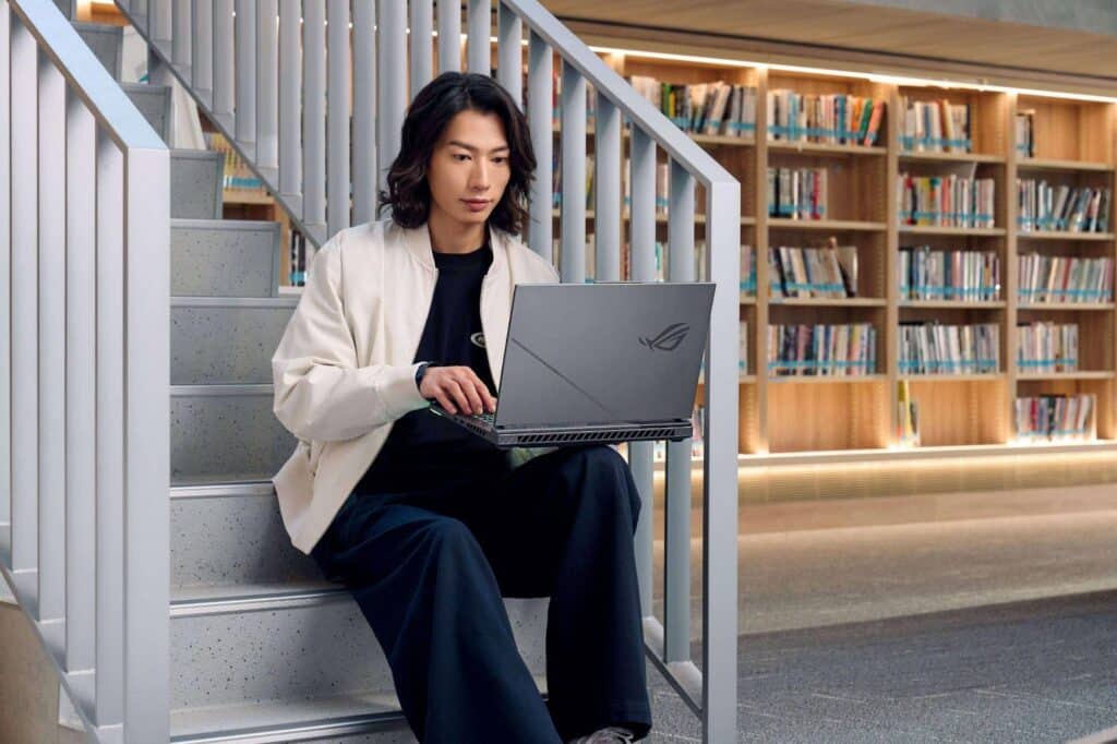 Jovem sentado em uma escada de uma biblioteca, usando um notebook ASUS.