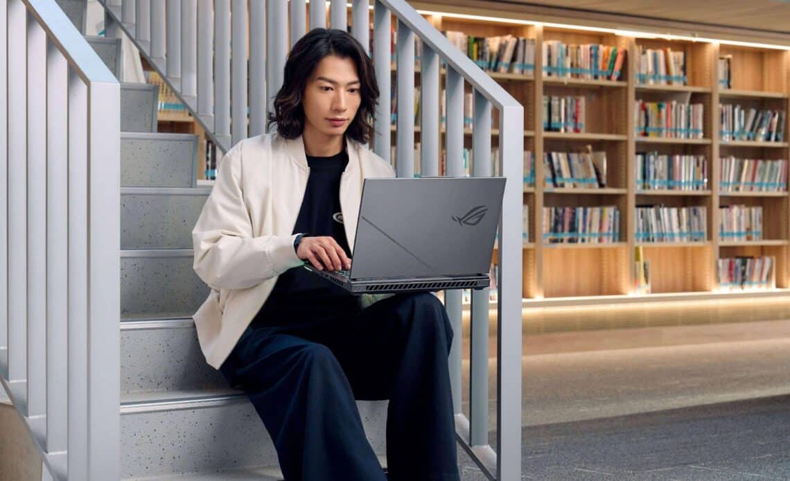 Jovem sentado em uma escada de uma biblioteca, usando um notebook ASUS.