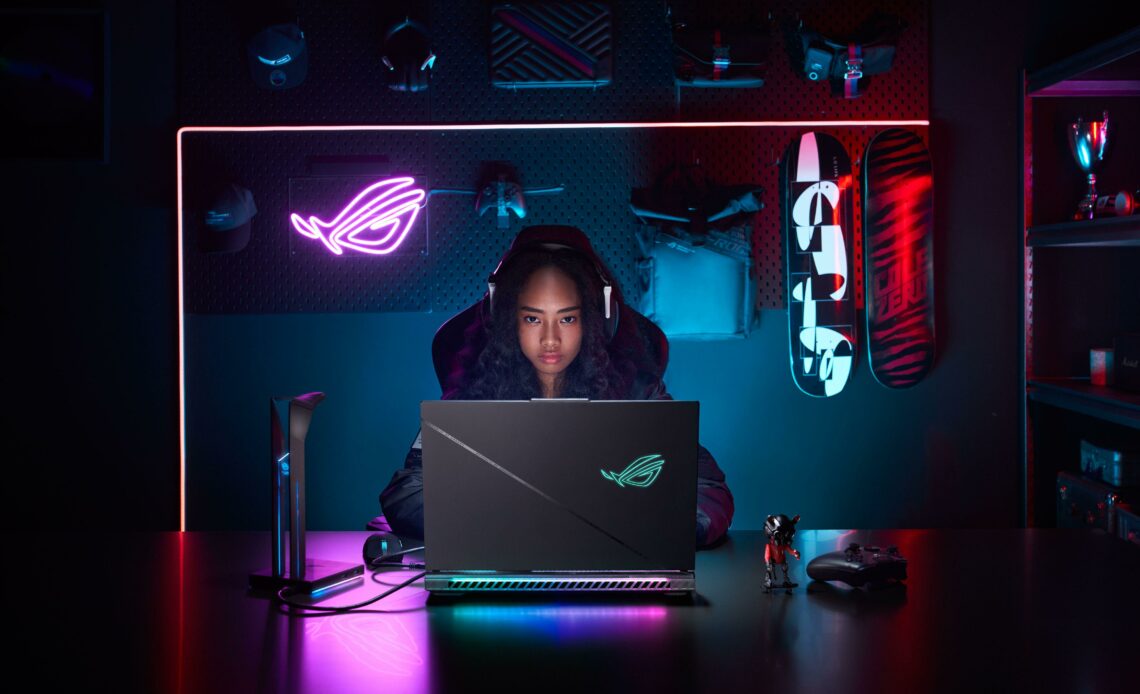 Jovem usando um notebook com iluminação neon em um ambiente moderno, com destaque para o ASUS ROG Strix Scar 18, ideal para jogos de alta performance.