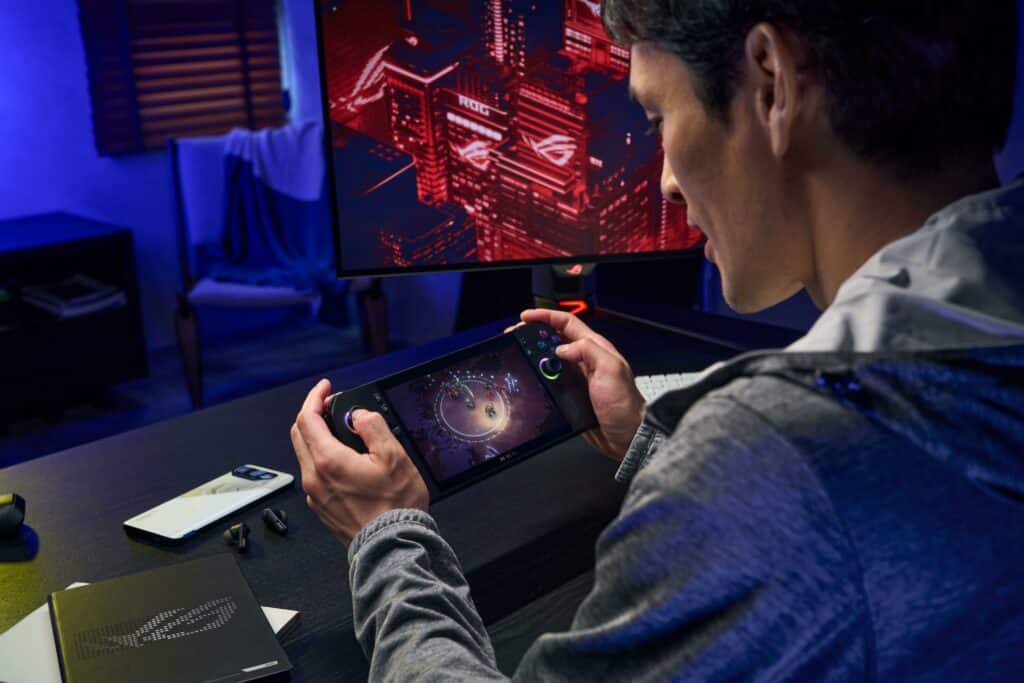 rog ally x nas mãos de um homem jogando diante de monitor ROG, em setup iluminado azul.
