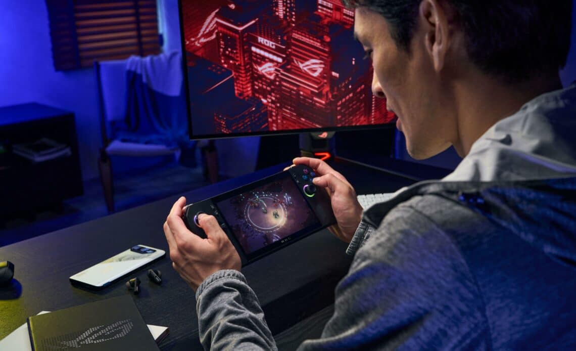 rog ally x nas mãos de um homem jogando diante de monitor ROG, em setup iluminado azul.